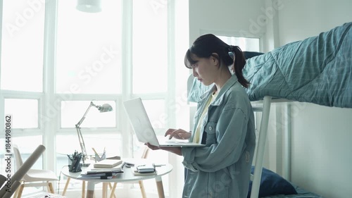 Asian girl standing holding laptop and typing on keyboard