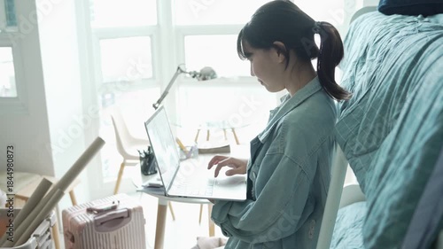 Asian girl standing holding laptop and typing on keyboard