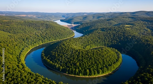 Aerial view captures a winding river forming a horseshoe bend surrounded by dense green forest slopes under clear sky