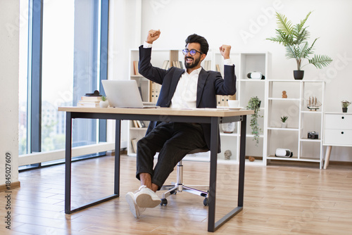 An Indian businessman celebrates a victory in his modern office, expressing joy and achievement