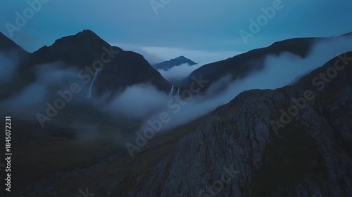 Dramatic view of rugged mountain peaks shrouded in low hanging mist and dark twilight clouds creating an atmospheric and mysterious landscape scene