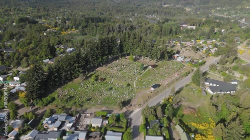 Aerial view of the cemetery in Villa La Angostura, Patagonia, Argentina, surrounded by forest and greenery. The image evokes themes of death, remembrance, religion, spirituality, and peaceful 