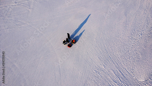 High-Angle Aerial View of Family Pulling a Tube Sled Across a Vast, Textured Snowfield