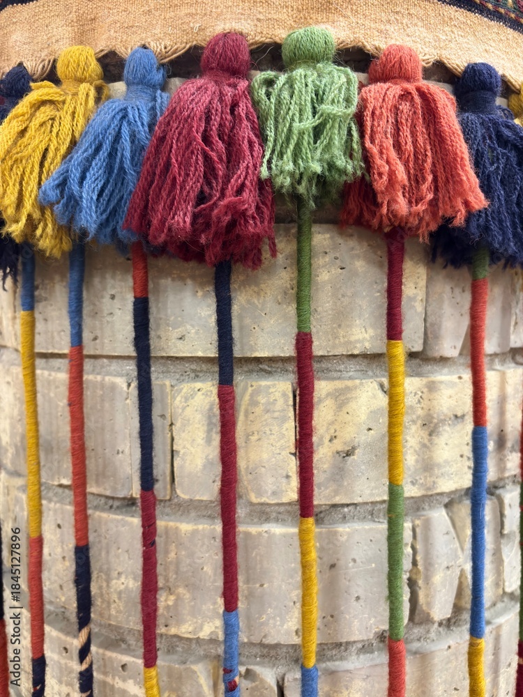 Obraz premium Colorful wool tassels on a traditional textile against a brick wall