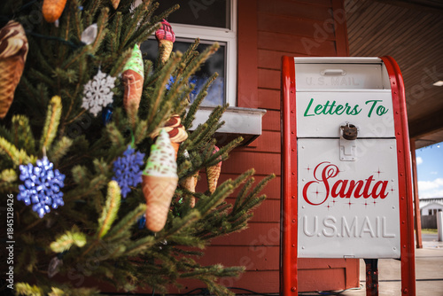 Santa mailbox beside a decorated Christmas tree with colorful ornaments in an outdoor holiday setting.