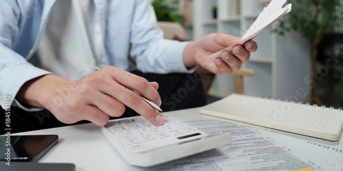 Tax Calculation. Man using calculator while holding receipts and financial documents.