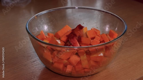 Preparing baked pumpkin in the oven, a delicious autumn dish made with pumpkin, feta cheese, and olive oil, a healthy and nutritious meal, with hands mixing the ingredients in a glass bowl.