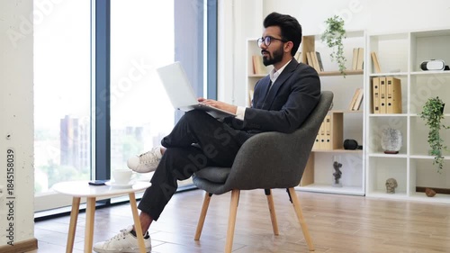 An Indian businessman is working on his laptop while sitting in a modern office setting