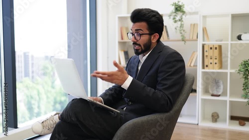 An Indian businessman smiles while giving a thumbs up during a video call on his laptop