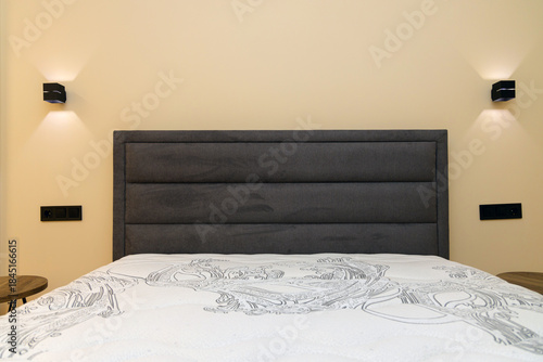 Bedroom interior: close-up of a double bed with a white orthopedic mattress. Modern bedside lamps are positioned on either side. The concept is one of comfort, sleep, minimalism, and interior design.