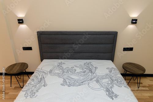 Bedroom interior: close-up of a double bed with a white orthopedic mattress. Modern bedside lamps are positioned on either side. The concept is one of comfort, sleep, minimalism, and interior design.