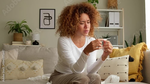 Sick woman having fever and measuring her temperature at home