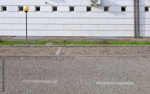 Fototapeta Naklejka Na Ścianę i Meble -  Elegant white stone tiled facade with small windows. Sidewalk, strip of grass and street in front. Background for copy space. 