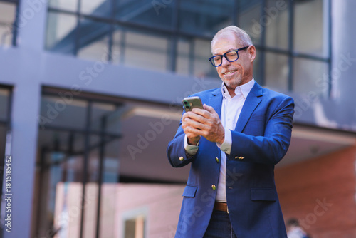 Mature businessman smiling using smartphone outdoors