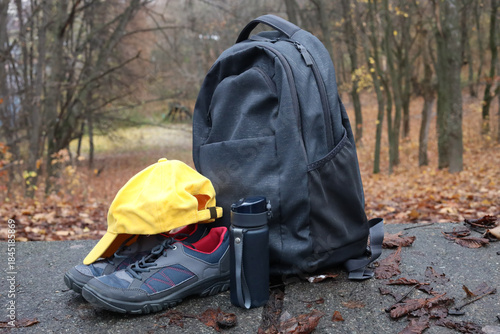 Tourist backpack, hiking boots, picnic utensils and hat on a path on the mountainside in the forest.
