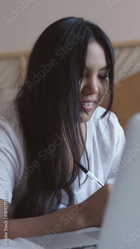 Young native american woman studying in bed with laptop and notebook