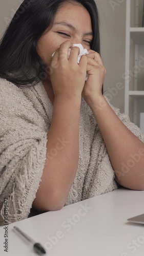 Sick hispanic woman blowing her nose with a tissue