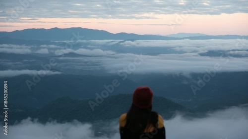 Rear view of a woman sitting and looking at a beautiful foggy mountain before sunrise