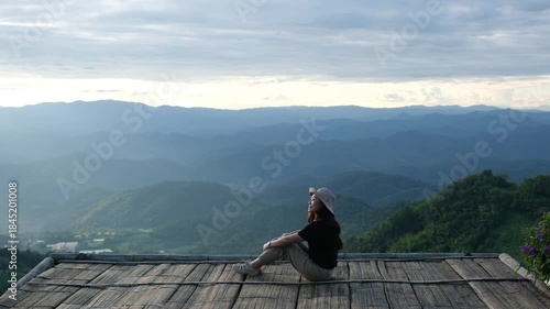 A woman sitting on wooden terrace and looking at a mountain view before sunset
