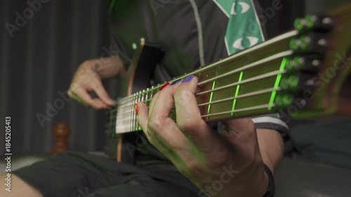 Close up of finger musician at the bass guitar , musician playing bass guitar in the room and with neon lights ,Bassist practicing in a bedroom studio.