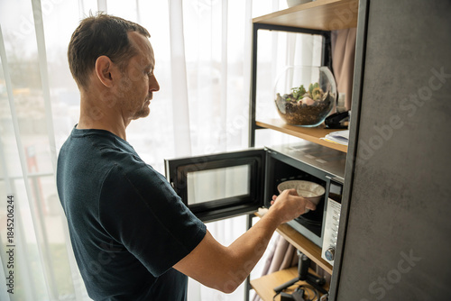 Man using a microwave oven in a home kitchen. Everyday food preparation.