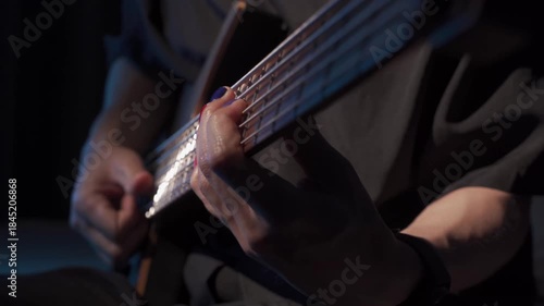 Close up of finger slap bass of musician at the bass guitar , musician playing bass guitar in the room and with neon lights ,Bassist practicing in a studio.