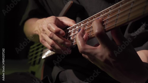 Close up of finger tapping bass of musician at the bass guitar , musician playing bass guitar in the room and with neon lights ,Bassist practicing in a studio.