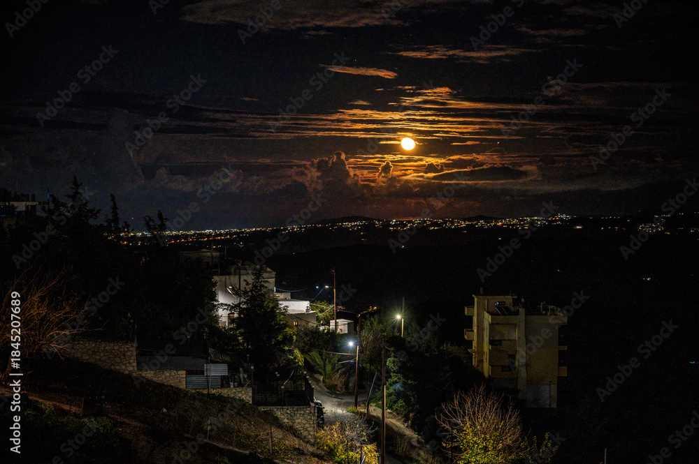 Fototapeta premium Night cityscape with full moon rising above clouds, dramatic sky, glowing urban lights, quiet hillside neighborhood, moody atmosphere, long exposure landscape, serene nocturnal scenery