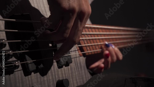 Close up of finger musician at the bass guitar , musician playing bass guitar in the room and with  spotlights ,Bassist practicing in a  studio.