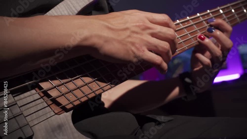 Close up of finger musician at the bass guitar , musician playing bass guitar in the room and with  spotlights and neon light ,Bassist practicing in a bedroom studio.
