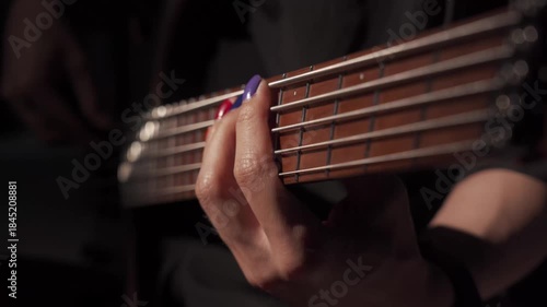 Close up of finger musician at the bass guitar , musician playing bass guitar in the room and with  spotlights ,Bassist practicing in a studio.