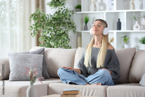 Blonde woman wearing headphone meditating at home