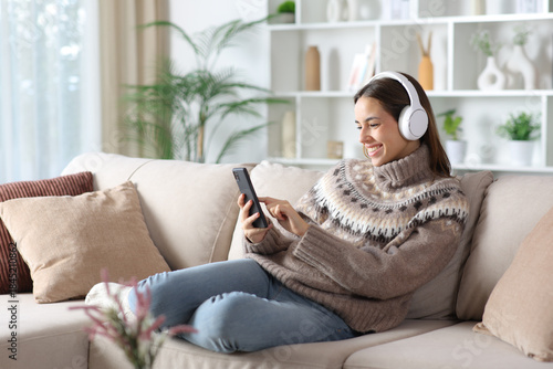 Happy woman listening audio in winter using phone