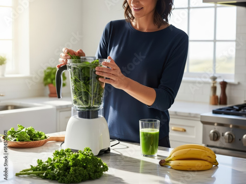 Woman adding fresh spinach to blender for healthy green smoothie in a bright kitchen