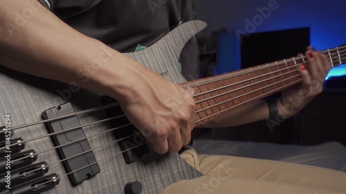 Close up of finger slap bass of musician at the bass guitar , musician playing bass guitar in the room and with neon lights ,Bassist practicing in a bedroom studio.