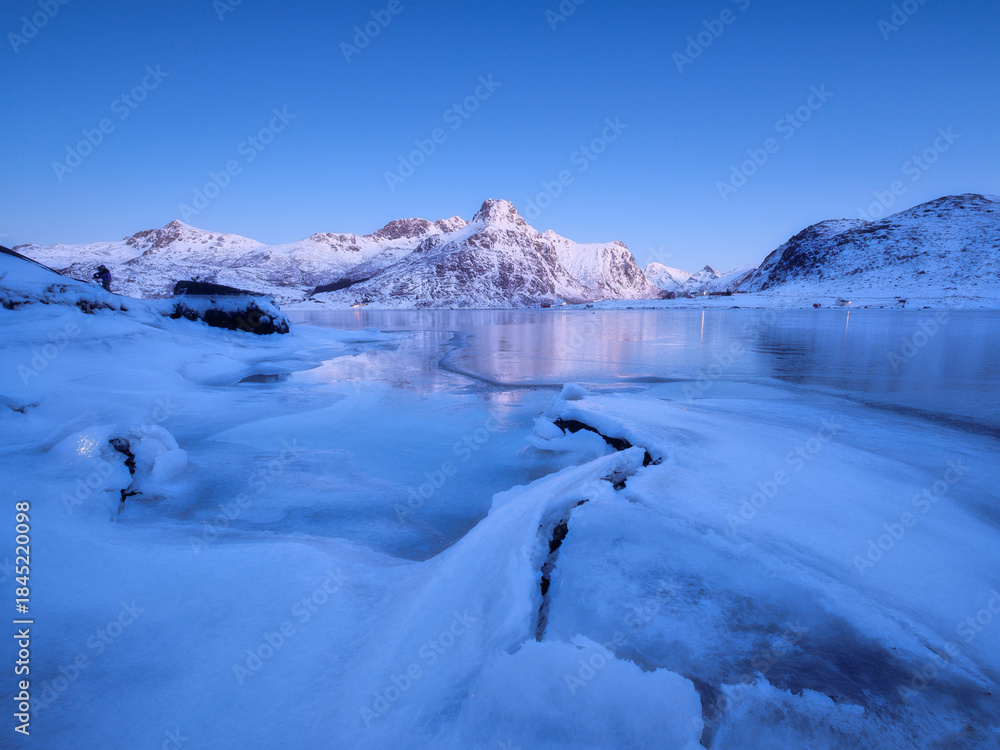 Obraz premium Lofoten islands, Norway. Nature in the fjords during winter night. Mountains, ice and reflections. Scandinavia. Vacation and travel in the winter north. Background, wallpaper, postcards.