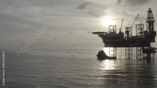 Aerial view from a drone of big jack up offshore drilling oil rig, production platform and supply vessel In the ocean during sunset - Oil and Gas Industry
