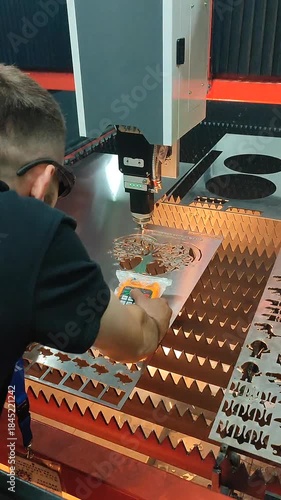 Male worker operating laser metal cutting machine. Man controlling machine with remote control. Laser cutting machine. Working process of laser cutting machine. Powerful laser beam cutting Vertical