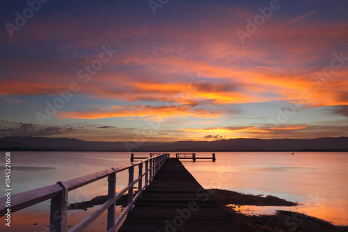 Tableau sur toile Sunset fills the sky with colour with beautifully vibrant colours over a jetty in a saltwater lake