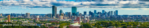Aerial view of the Boston skyline, a tapestry of glass towers and lush greenery under a vast, cloud-strewn sky, Boston, Massachusetts, United States.