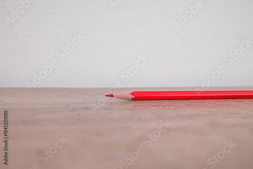 Sharp Red Colored Pencil Resting Horizontally on Textured Wooden Surface Against Bright