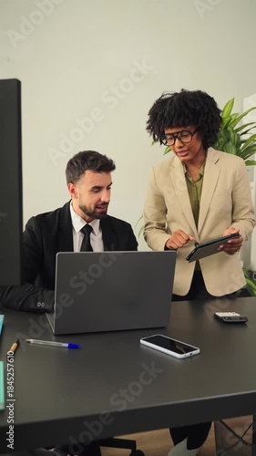 Two focused business professionals actively collaborating and discussing ideas while working in a stylish office space with a laptop and tablet on the desk. The atmosphere is productive and energetic.