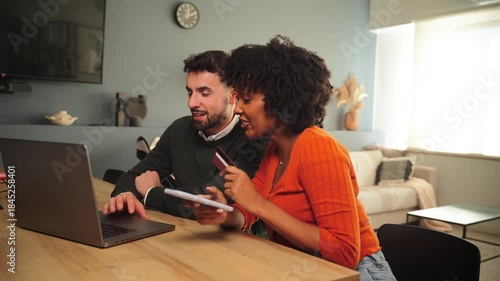 A happy couple engaged in online shopping together using a laptop and a credit card in their cozy home. They are excited about their purchases and enjoying the process of shopping together.
