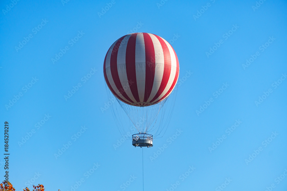 Naklejka premium A hot air balloon as a viewing platform for tourists is flying high in the sky above the treetops in Budapest, Hungary.