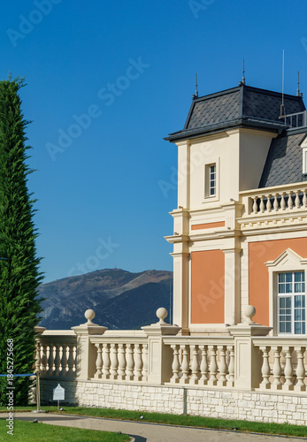 Classical building of Chateau de Talyu winery with decorative balustrade and tower under blue sky against majestic mountains rise, adding to scenic beauty. Gelendzhik, Russia - September 30, 2024