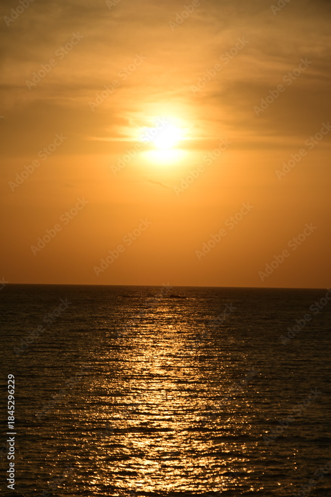 Fototapeta premium A breathtaking tropical seascape during the golden hour or sunset, featuring a dramatic sun flare and long, bright reflection path across the ocean surface