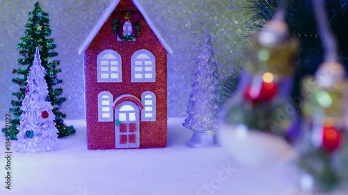 On a light brown background, an orange-blue house with Christmas trees nearby and large lights decorated inside in the foreground