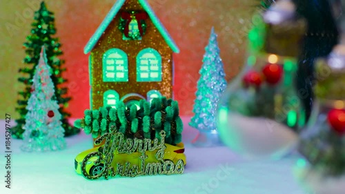 On a light brown background, an orange-blue house surrounded by Christmas trees and a car with letters in front and large lights decorated inside in the foreground