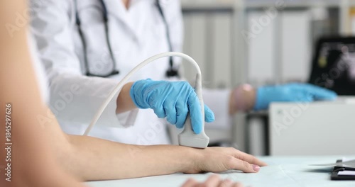 Medical worker in gloves presses ultrasound probe on female forearm and wrist. Specialist scans blood vessels on monitor checking circulation status
