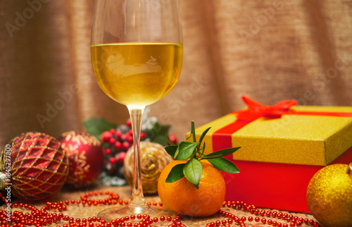 A glass of wine and a tangerine next to a gift in a box with Christmas tree balls